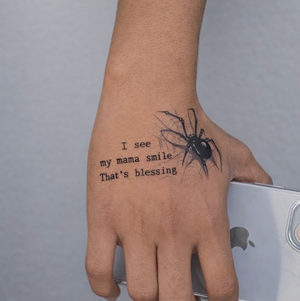 12 Spider Tattoo Ideas That Balance Creepy and Beautiful 5 A spider and web tattoo on a hand with sentimental text printed in black ink.