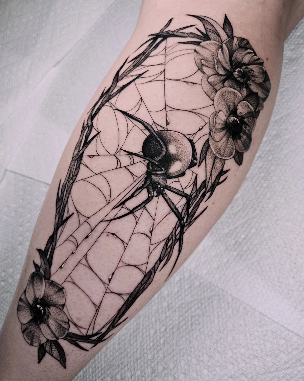 12 Spider Tattoo Ideas That Balance Creepy and Beautiful 9 A black and grey spider web tattoo with flowers on a person's leg.
