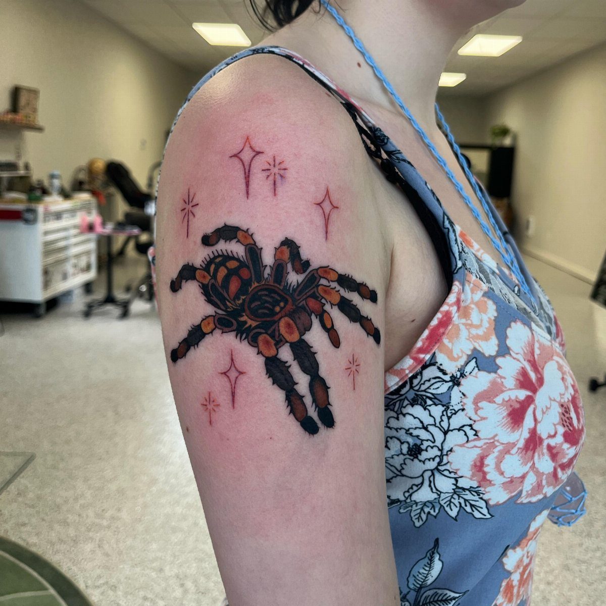 12 Spider Tattoo Ideas That Balance Creepy and Beautiful 8 A spider tattoo with orange accents and red sparkles on a person's upper arm.