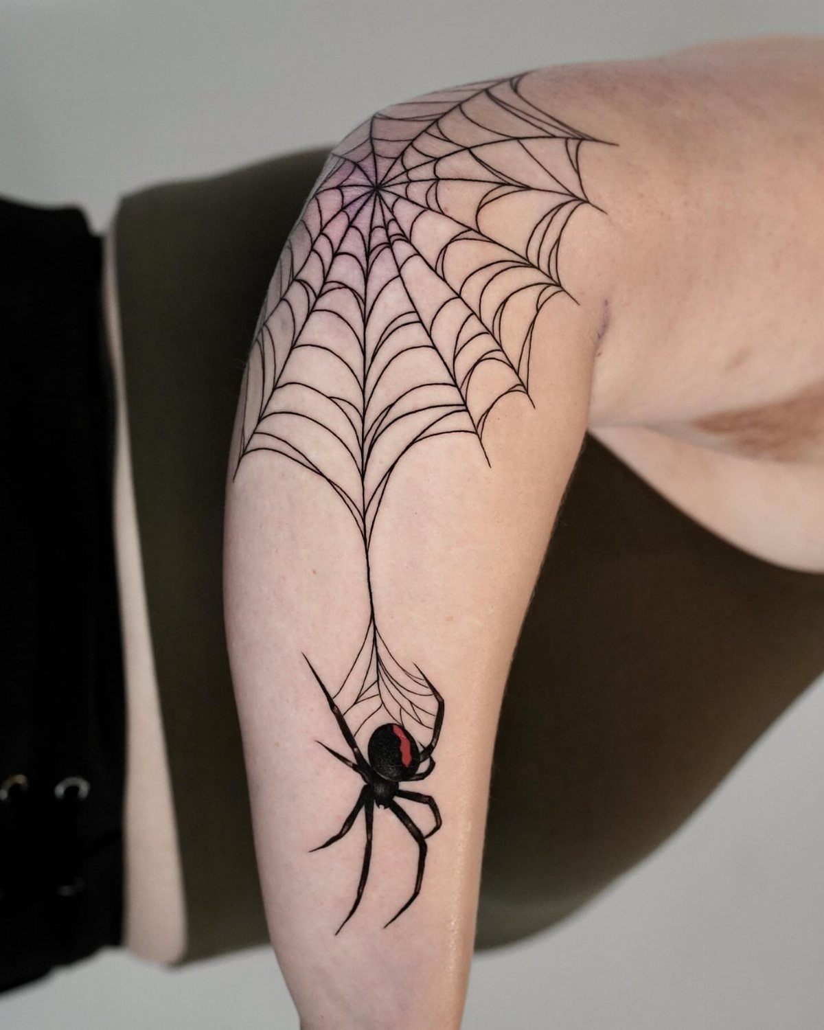 12 Spider Tattoo Ideas That Balance Creepy and Beautiful 4 A black ink spider and web tattoo on a person's upper arm.