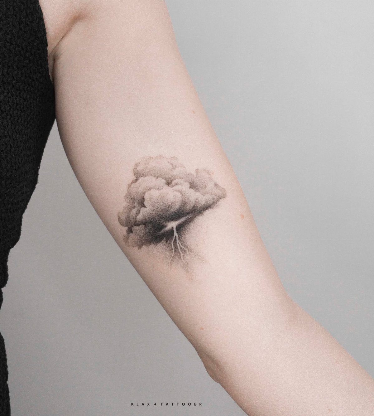 Storm Tattoo: 8 Nature-Inspired Designs for Your Next Ink 6 A black and grey realism tattoo of a large storm cloud with a lightning bolt on a person's arm.