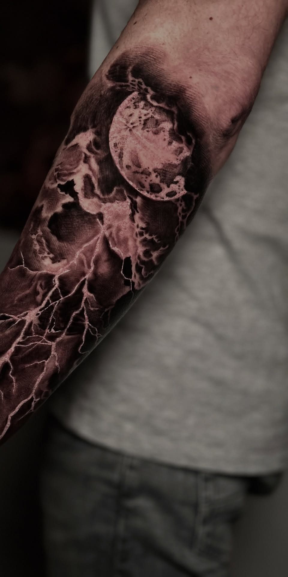 Storm Tattoo: 8 Nature-Inspired Designs for Your Next Ink 3 A detailed black and grey tattoo of a full moon with lightning and storm clouds on an arm.