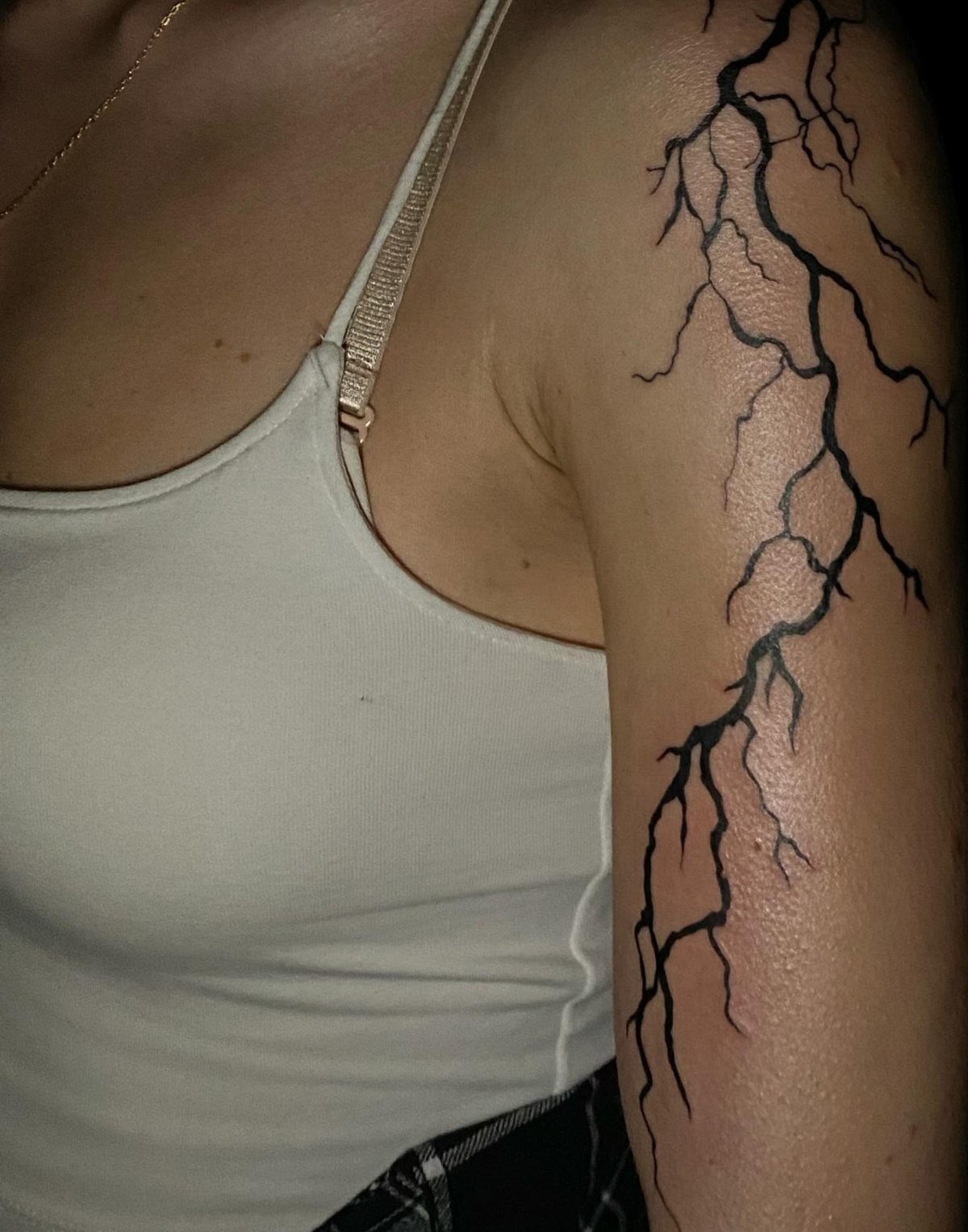 Storm Tattoo: 8 Nature-Inspired Designs for Your Next Ink 2 A black ink lightning bolt tattoo branching down a person's upper arm.