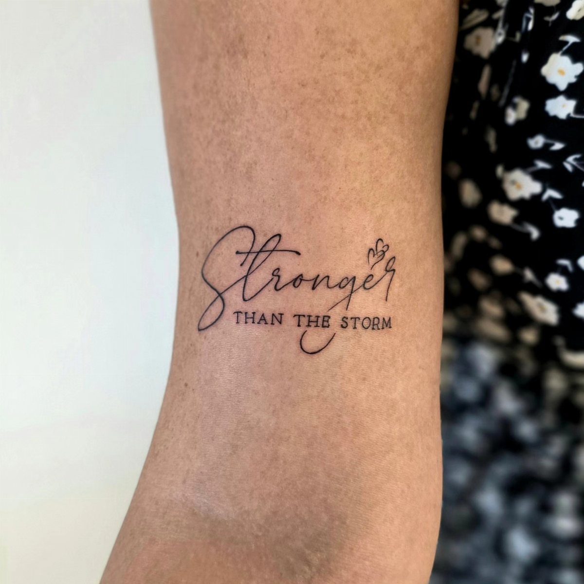 Storm Tattoo: 8 Nature-Inspired Designs for Your Next Ink 4 A black ink text tattoo on a person's forearm reading Stronger than the storm.