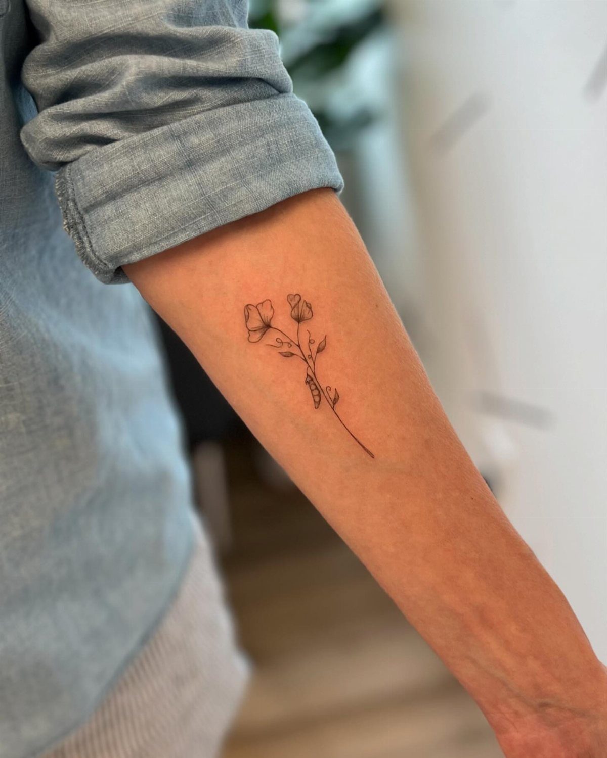 Sweet Pea Flower Tattoo: 7 Ideas for Placement and Style 1 A fine line black ink sweet pea flower tattoo on a person's forearm.
