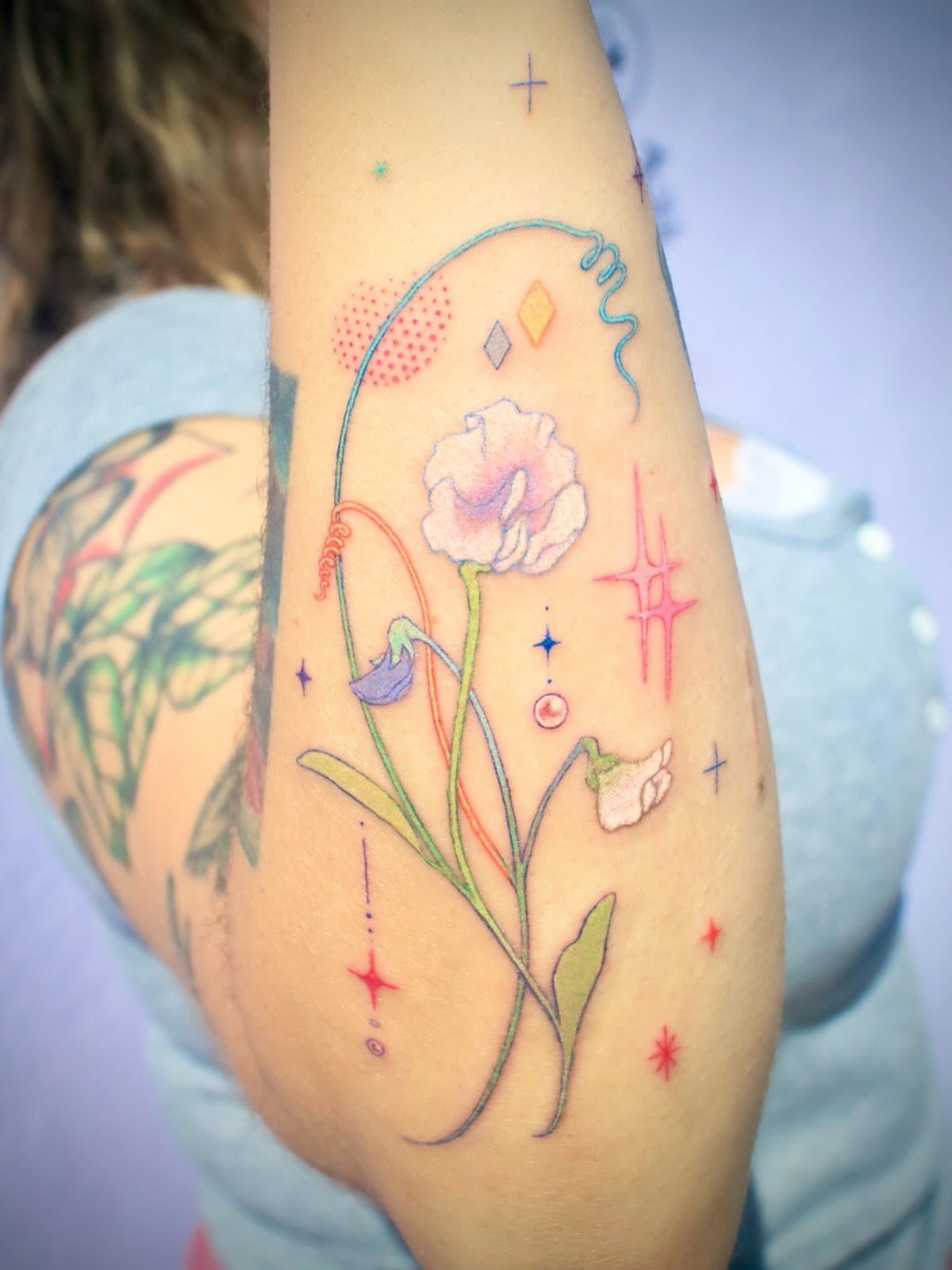 Sweet Pea Flower Tattoo: 7 Ideas for Placement and Style 3 A colorful sweet pea flower tattoo with swirling lines and stars on a person's arm.