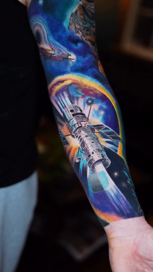 7 Telescope Tattoo Ideas for Every Space and Style 6 A colorful sleeve tattoo of a space telescope amidst a vibrant, swirling cosmic nebula.