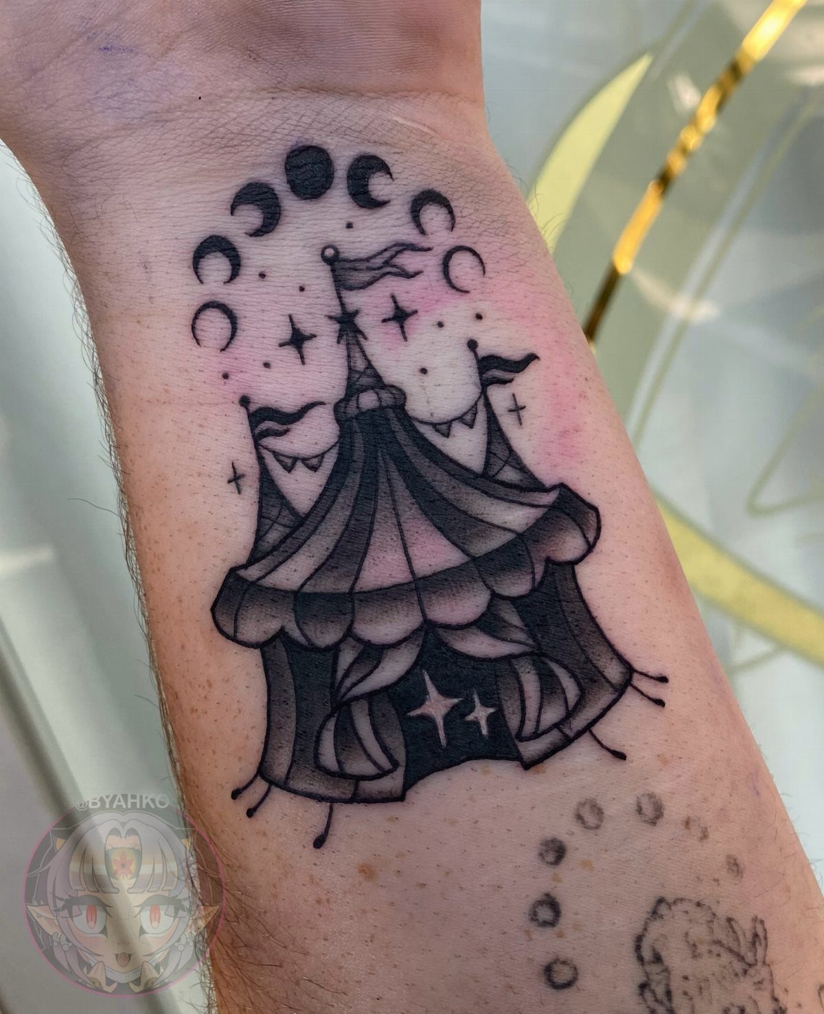 6 Tent Tattoo Ideas for Camping and Circus Styles 6 A black and grey circus tent tattoo with moons and stars on a person's forearm.