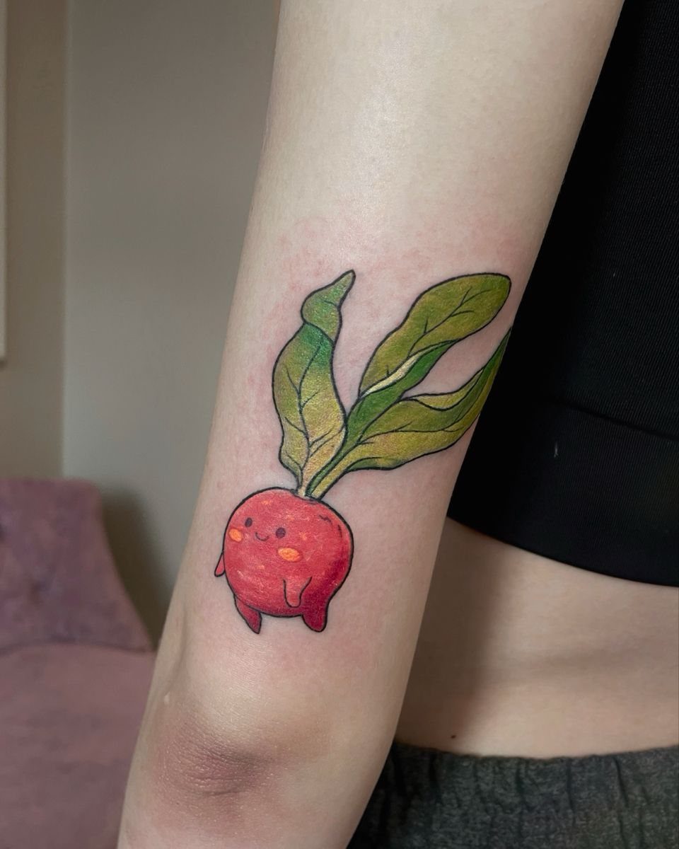 The Most Beautiful Radish Tattoo: 8 Designs for Your Next Ink 2 A small red radish character tattoo with a smiling face and green leaves on an arm.