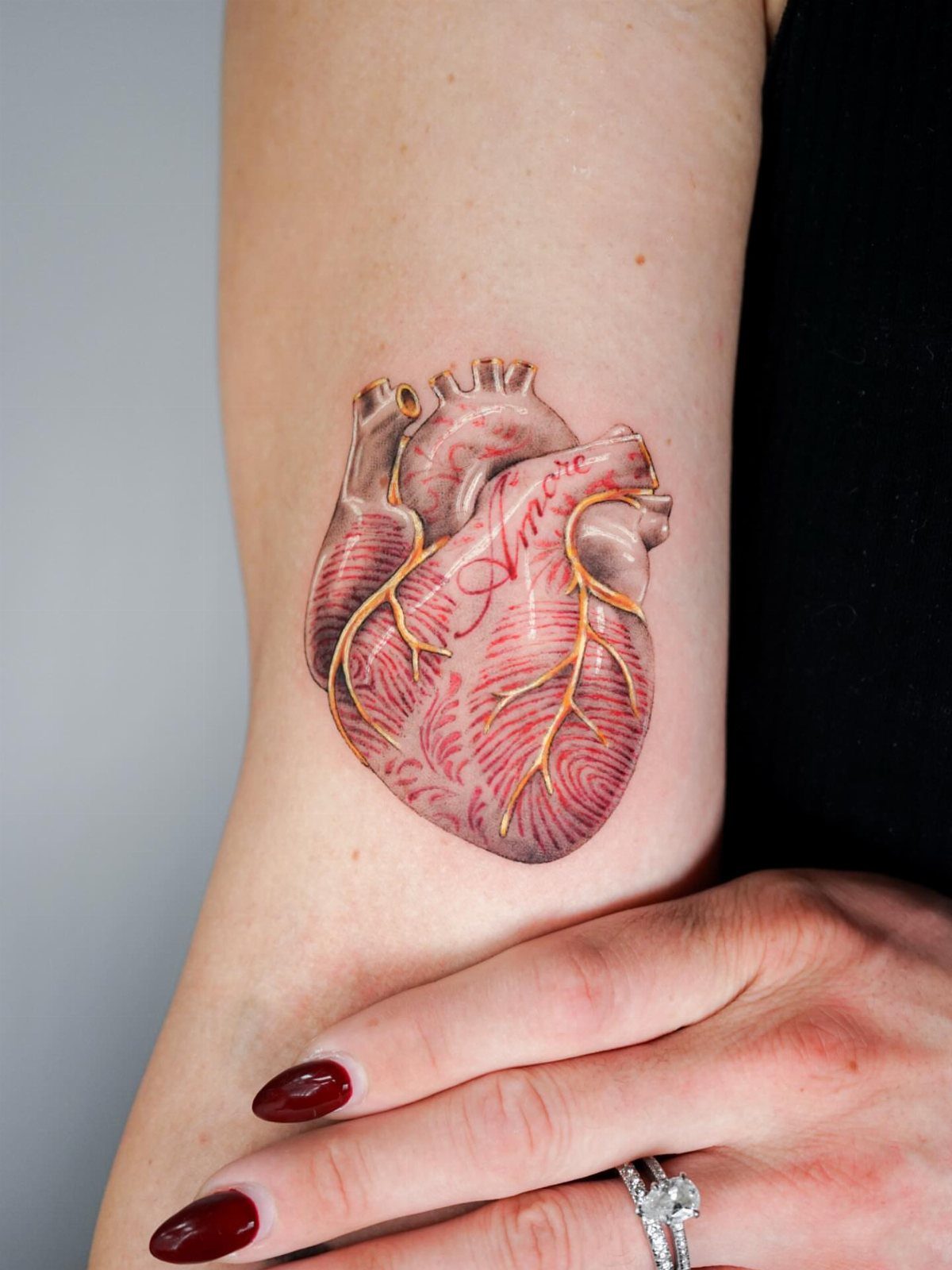 6 Thumbprint Heart Tattoo Ideas to Seal a Bond in Ink 5 Anatomical heart tattoo with red and gold veins on a person's forearm.