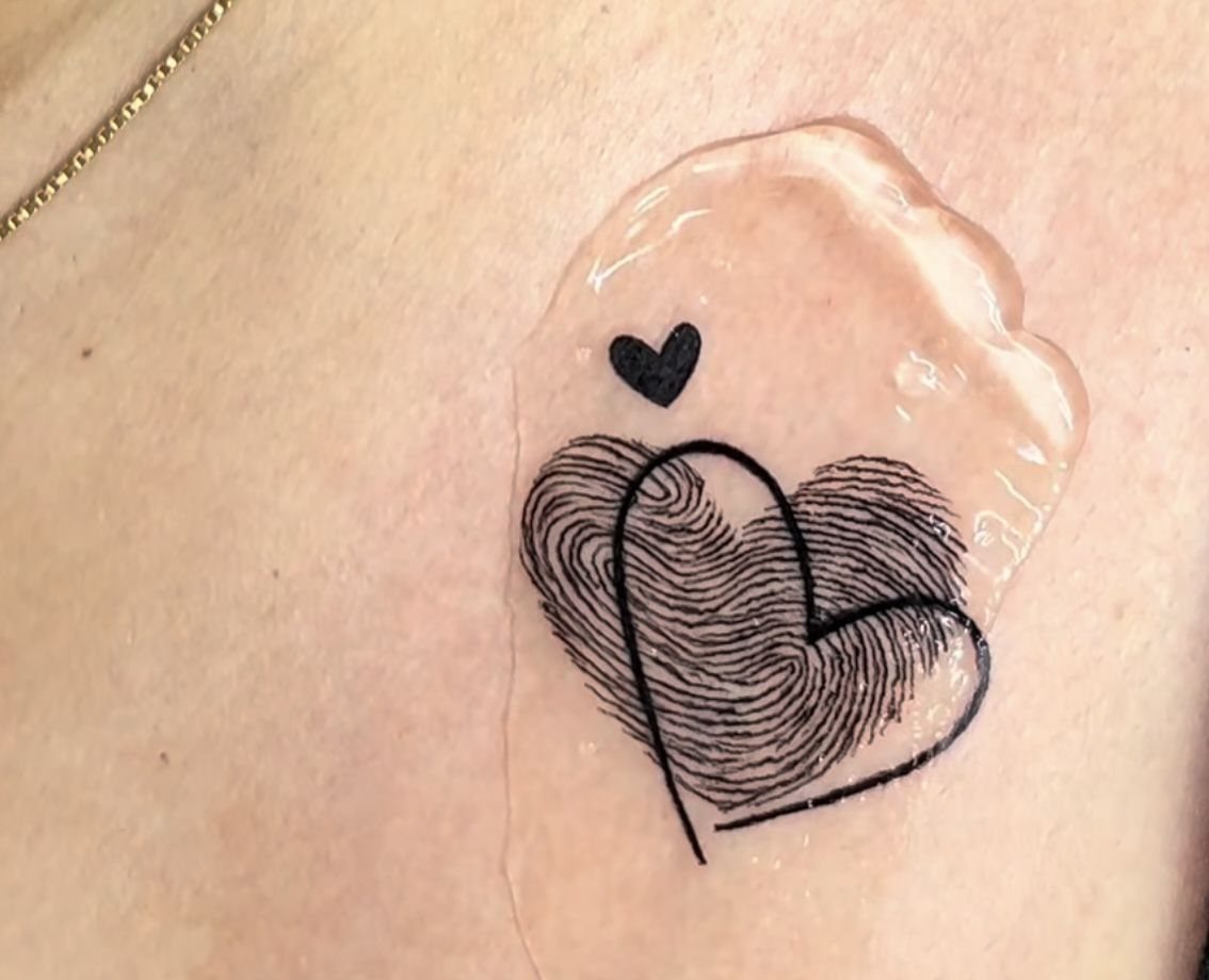 6 Thumbprint Heart Tattoo Ideas to Seal a Bond in Ink 6 Two overlapping thumbprint heart tattoo with a small black heart above it on skin.