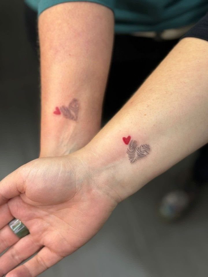 6 Thumbprint Heart Tattoo Ideas to Seal a Bond in Ink 4 Two wrists displaying small thumbprint heart tattoos with tiny red hearts.