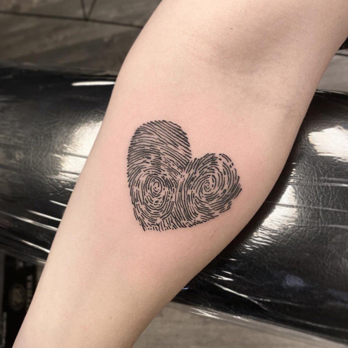 6 Thumbprint Heart Tattoo Ideas to Seal a Bond in Ink 1 A black ink heart tattoo made from two fingerprint patterns on a person's arm.