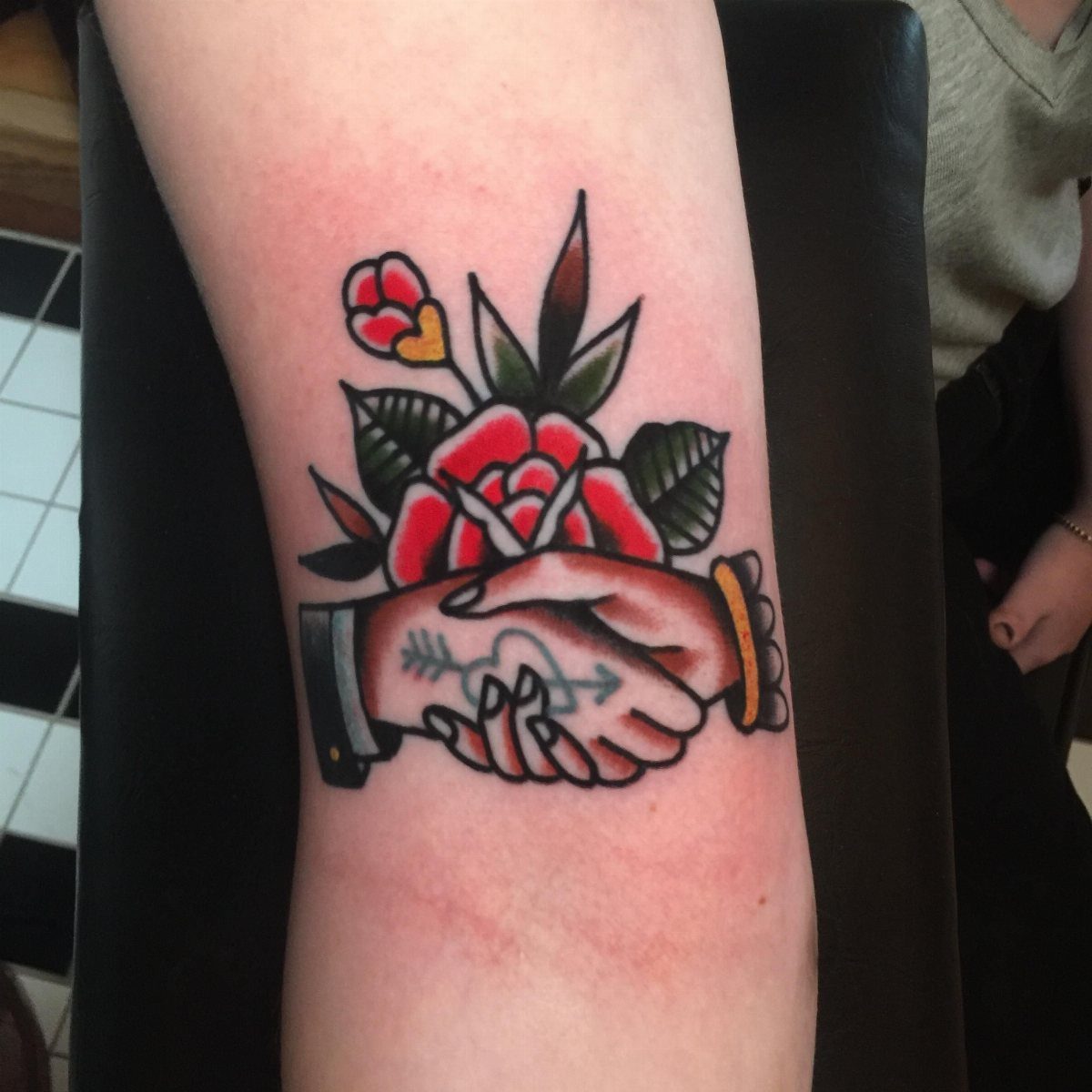 Traditional Handshake Tattoo: 9 Designs From Heart Frames to Skeleton Hands 7 Traditional tattoo of hands shaking with a rose and an arrow through a heart on an arm.