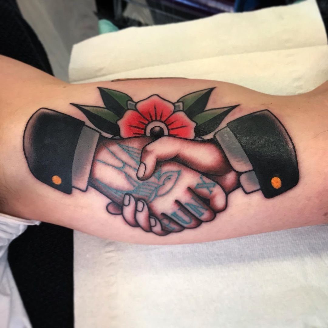 Traditional Handshake Tattoo: 9 Designs From Heart Frames to Skeleton Hands 2 American traditional tattoo of two hands shaking with a red rose and swallows on an arm.
