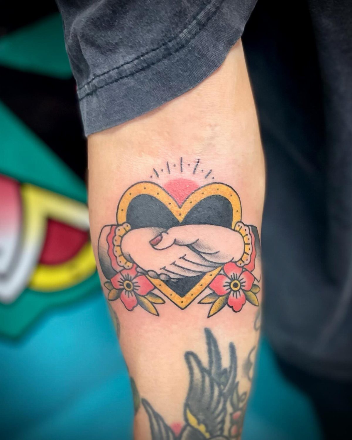 Traditional Handshake Tattoo: 9 Designs From Heart Frames to Skeleton Hands 1 A traditional tattoo of two hands shaking inside a heart frame with pink flowers.