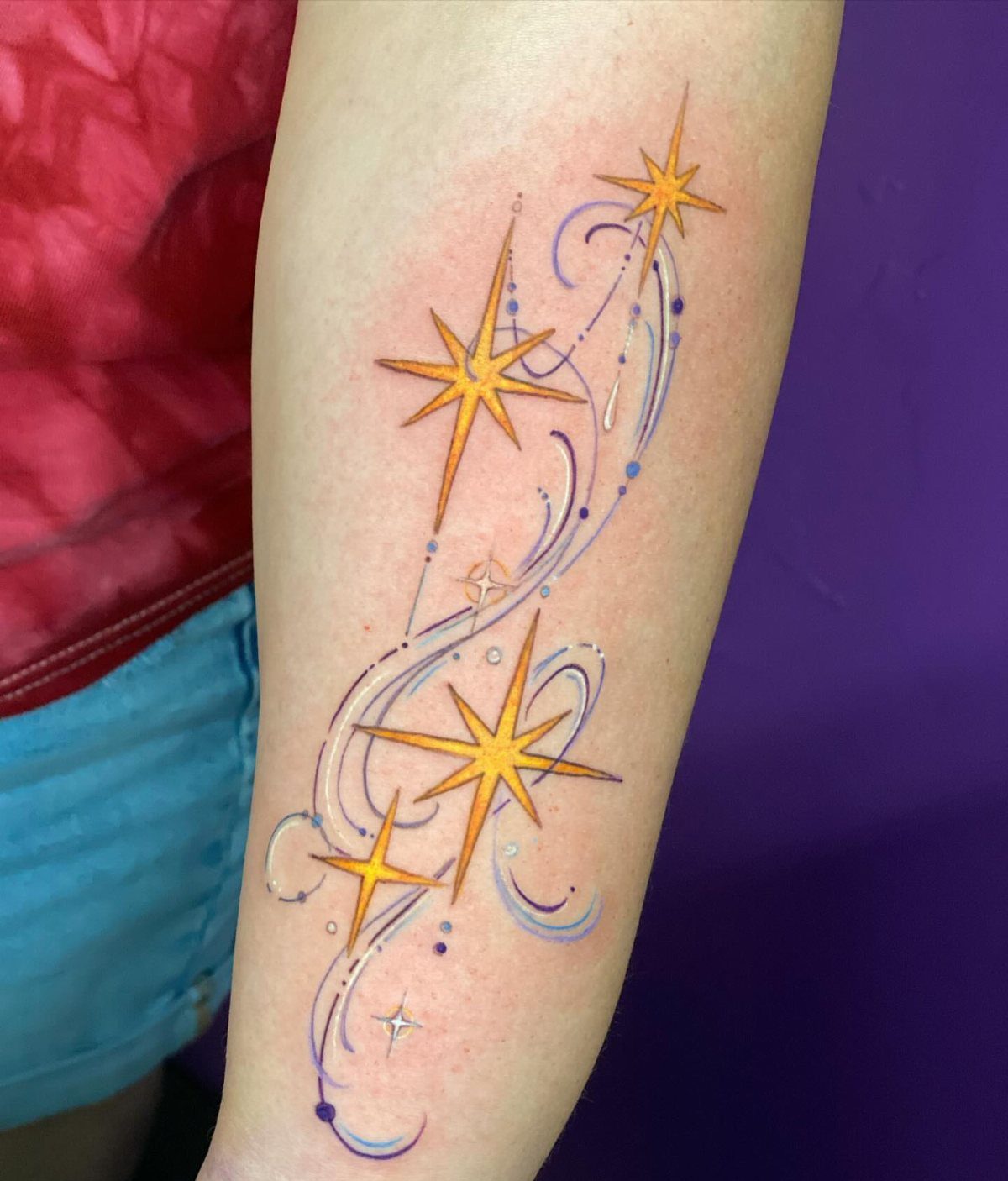 6 Twinkle Star Tattoo Ideas for Light, Sparkly Ink 6 A cosmic tattoo of yellow stars and blue swirling lines on a person's arm.