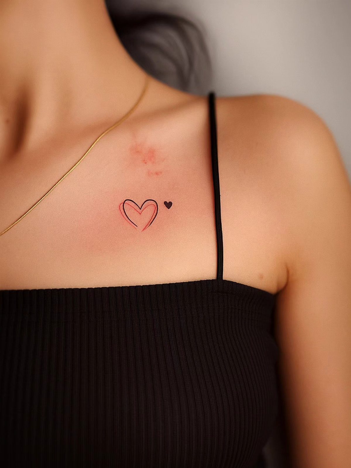 7 Unconditional Love Tattoo Ideas for Quiet, Lasting Ink 7 A small red heart outline tattoo with a tiny black heart on a person's collarbone.