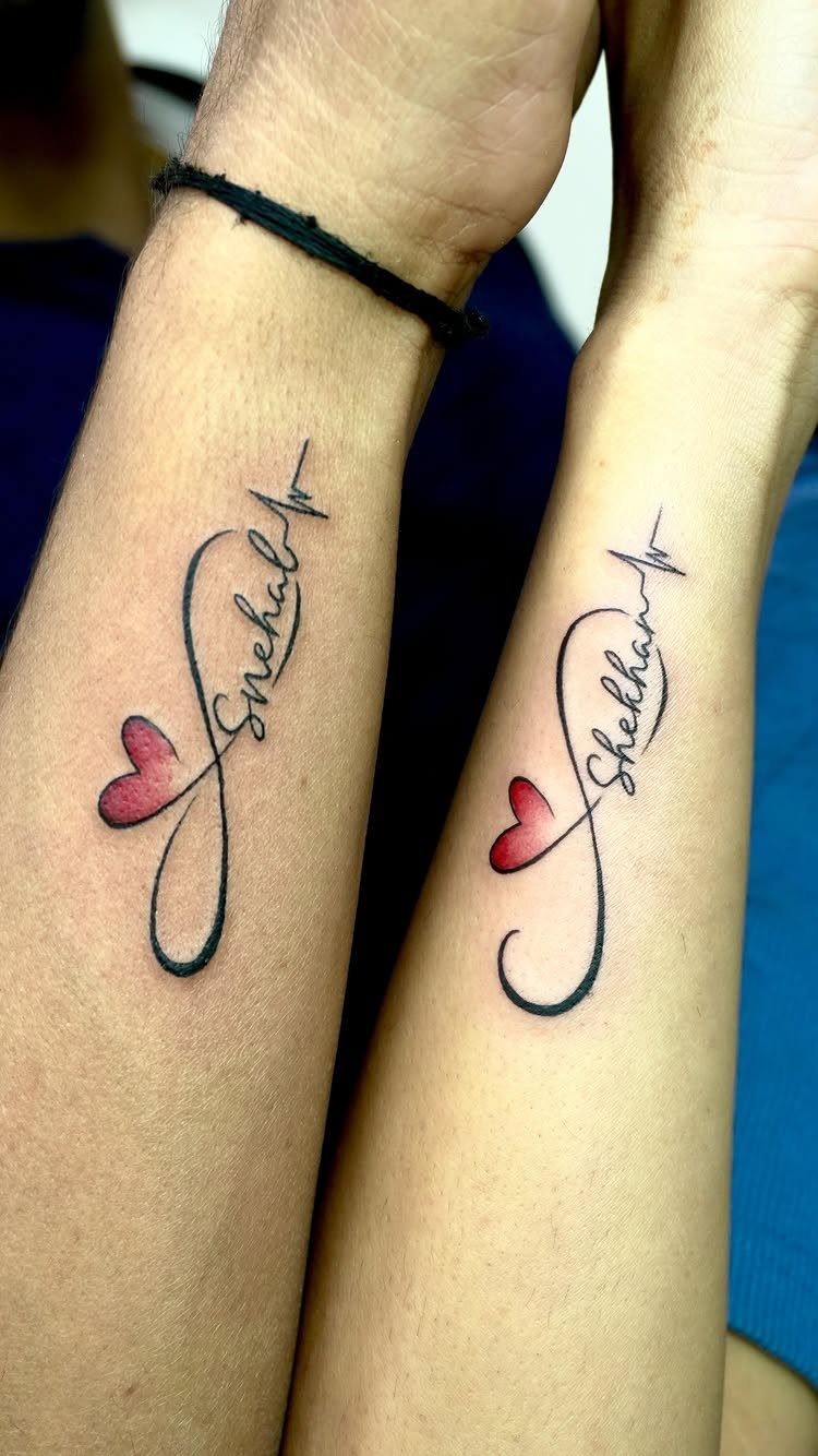 7 Unconditional Love Tattoo Ideas for Quiet, Lasting Ink 2 Two forearms displaying matching infinity symbol tattoos with red hearts and cursive names in black ink.
