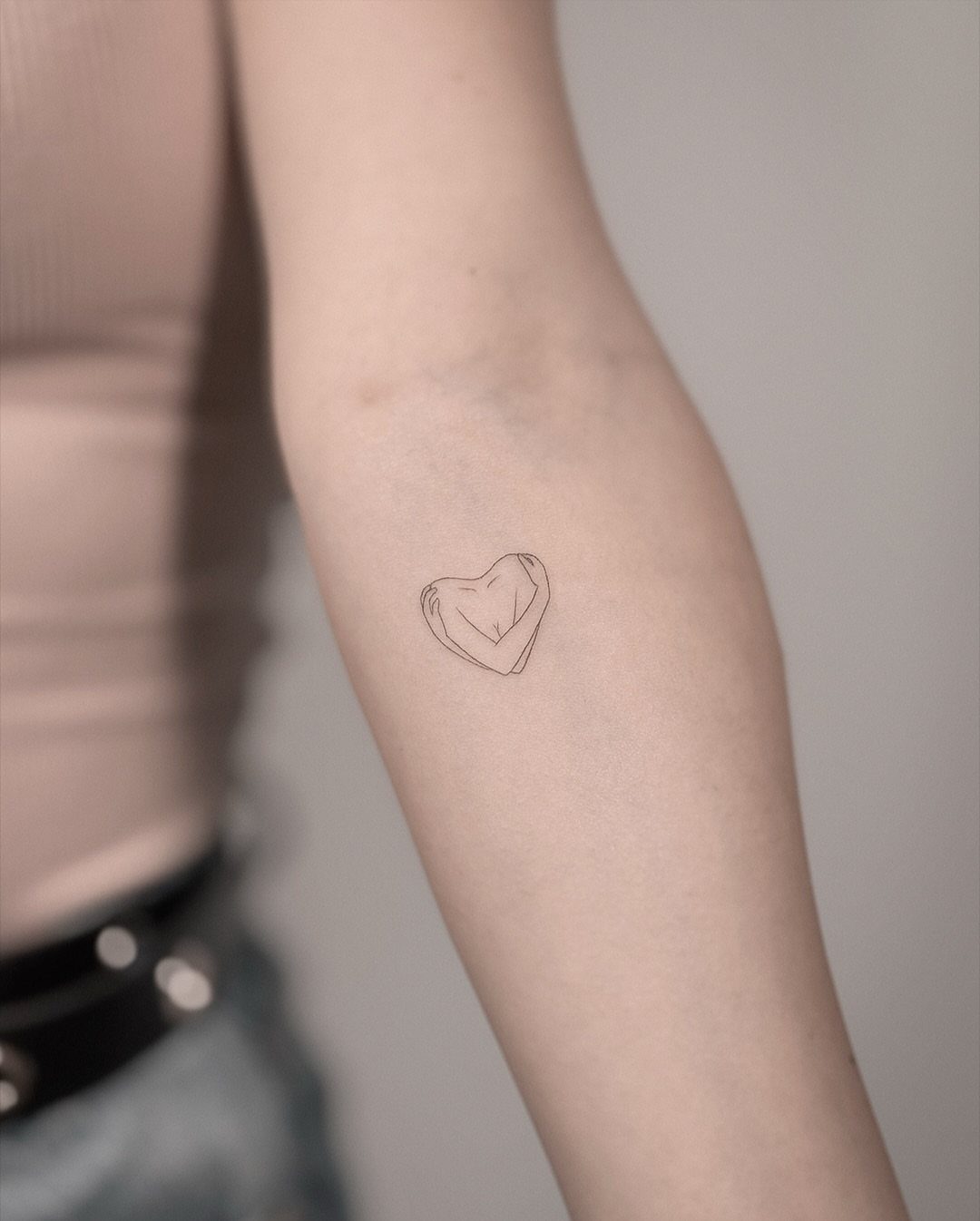 7 Unconditional Love Tattoo Ideas for Quiet, Lasting Ink 6 A small minimalist fine-line heart tattoo on a person's inner forearm.
