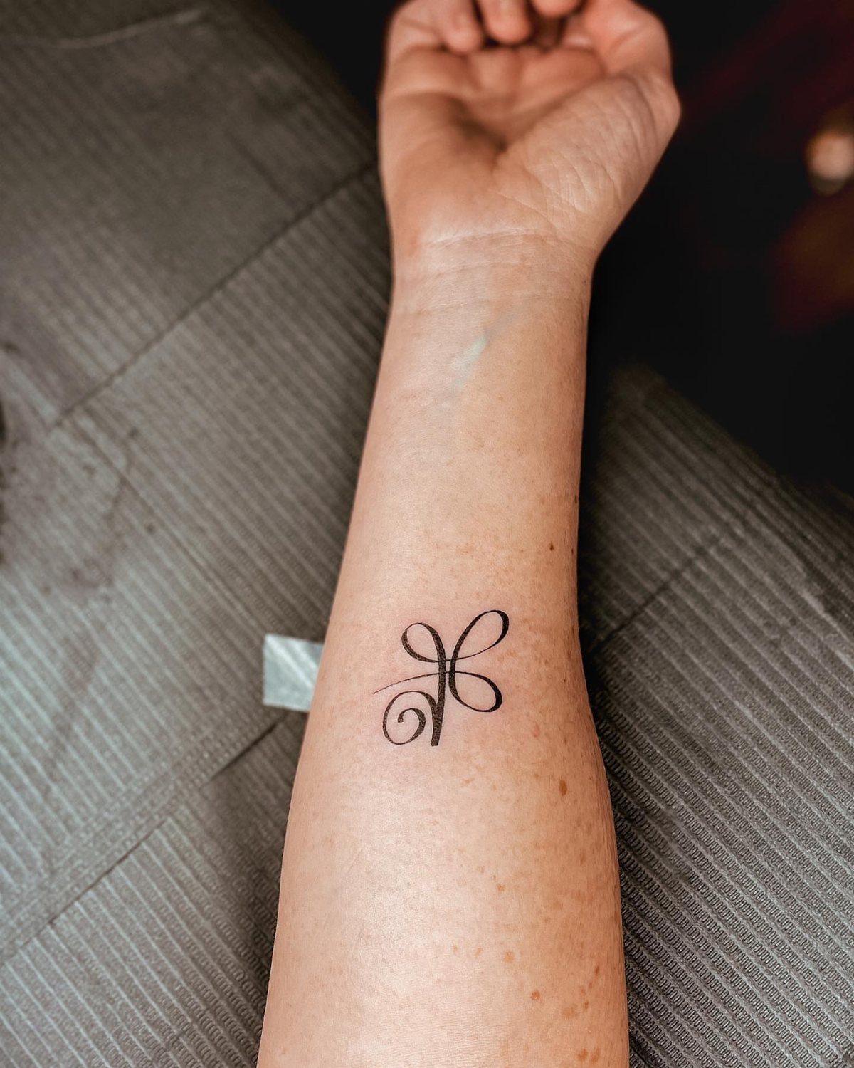 7 Unconditional Love Tattoo Ideas for Quiet, Lasting Ink 1 A minimalist black line art loop tattoo on a person's inner forearm.