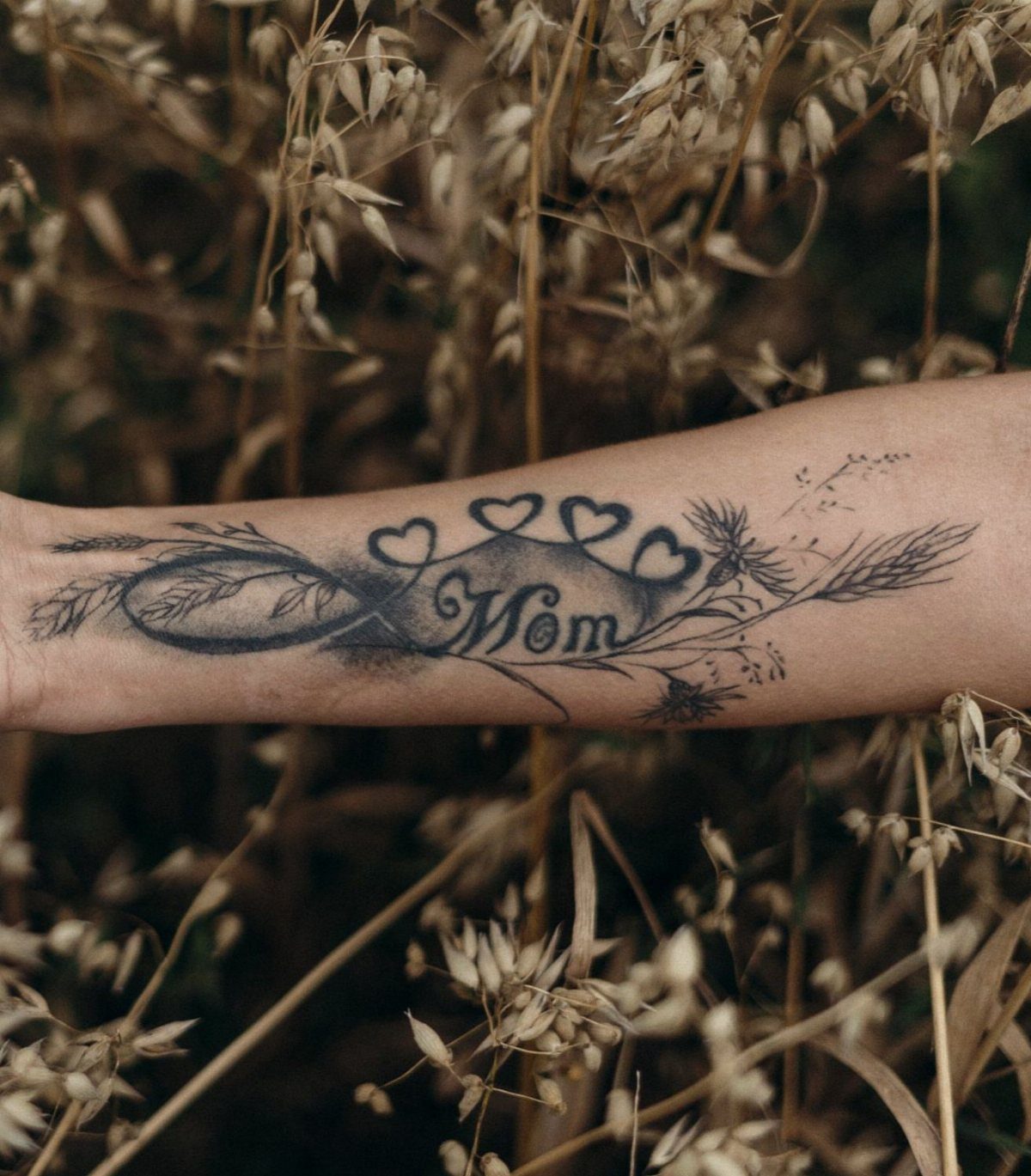 6 Wheat Tattoo Ideas for Your Next Ink 3 A forearm tattoo featuring an infinity symbol, wheat stalks, hearts, and the word Mom.