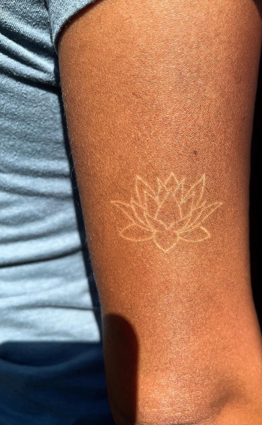 White Ink Water Lily Tattoo: 7 Ideas for Subtle Floral Ink 2 A delicate white ink lotus flower tattoo on a person's arm in bright sunlight.