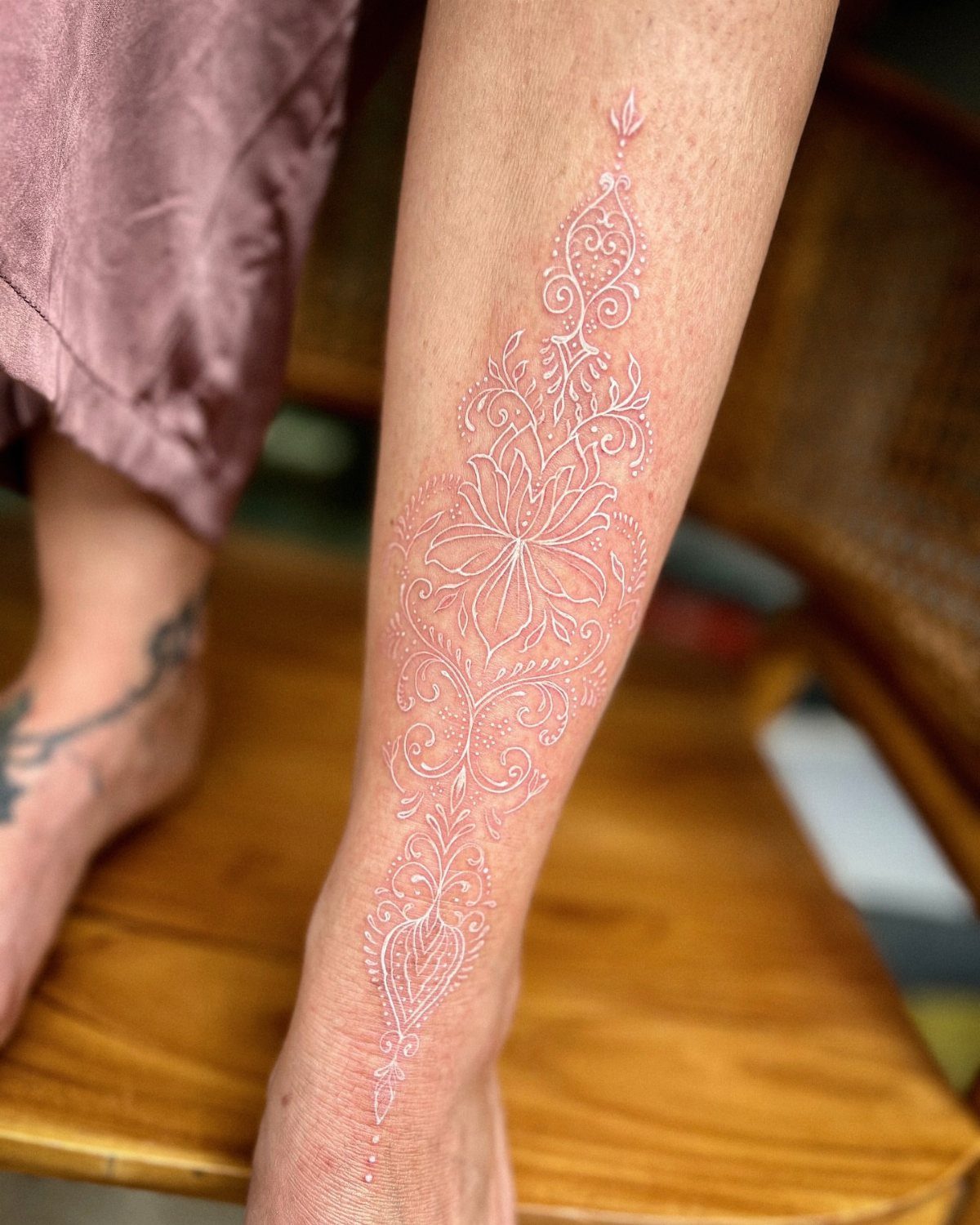 White Ink Water Lily Tattoo: 7 Ideas for Subtle Floral Ink 6 A detailed white ink tattoo of a water lily and ornamental swirls on a person's leg.